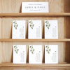 Set of white seating cards with names and table numbers on a wooden shelf with a title card at the top.