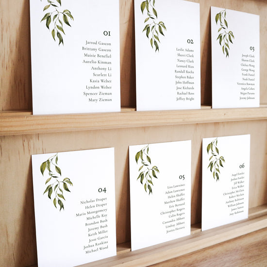 Set of six printable seating chart cards with names on a wooden display shelf.