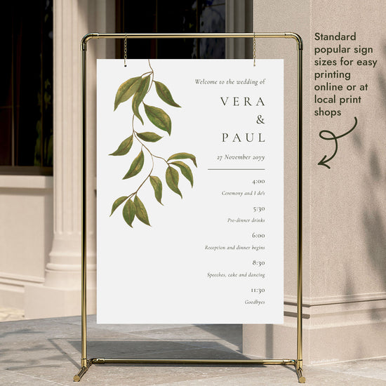 A wedding timeline sign template hung on a gold display stand outside a modern city building entrance