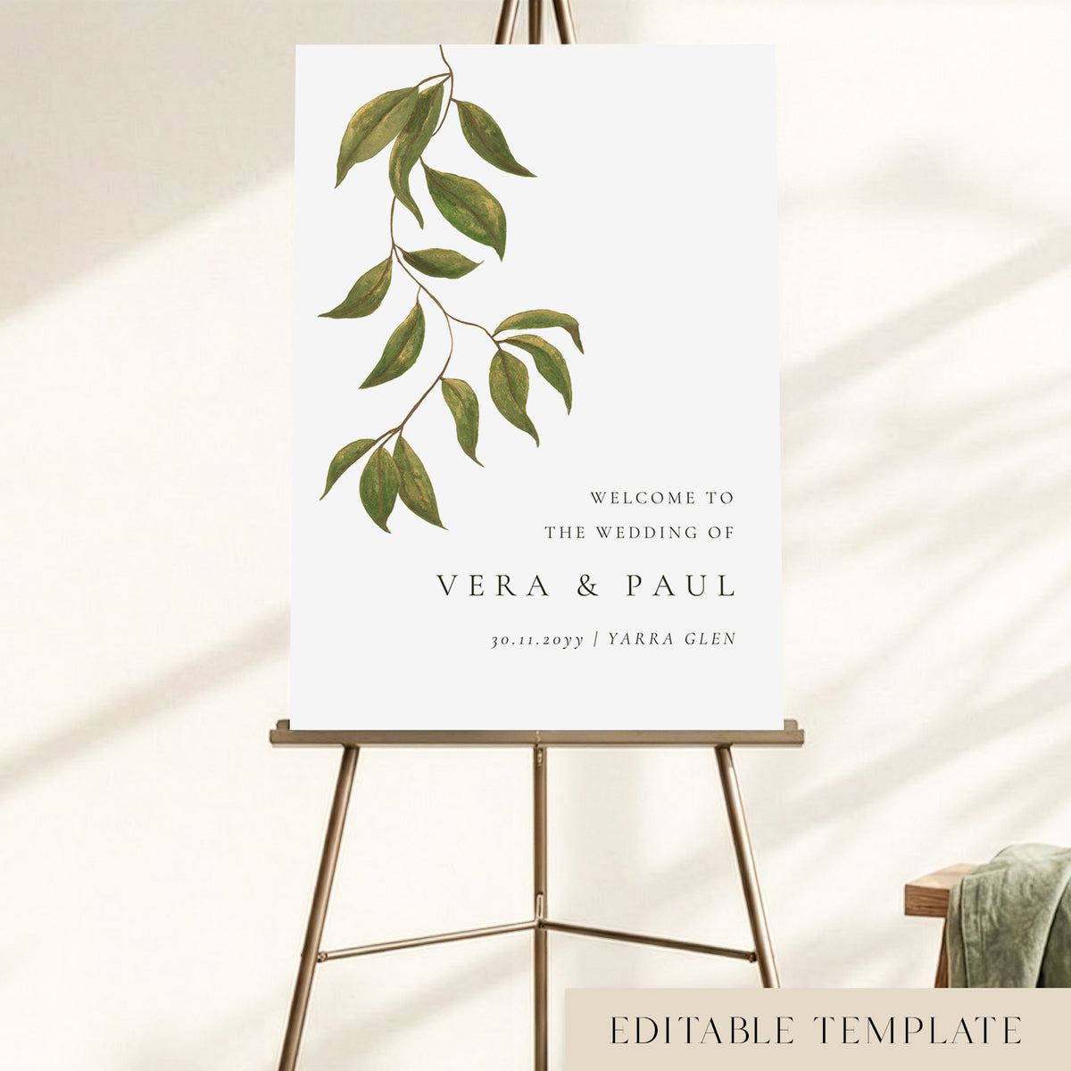 A wedding welcome sign displayed on an easel, with hand-painted greenery and the couple's names