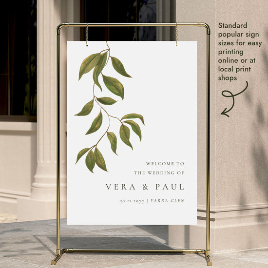 A wedding welcome sign template hung on a gold display stand outside a modern city building entrance