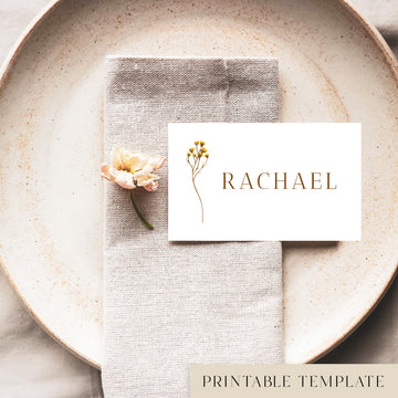A flat place card with a name printed on it, positioned on a plate with a napkin and a floral decoration.