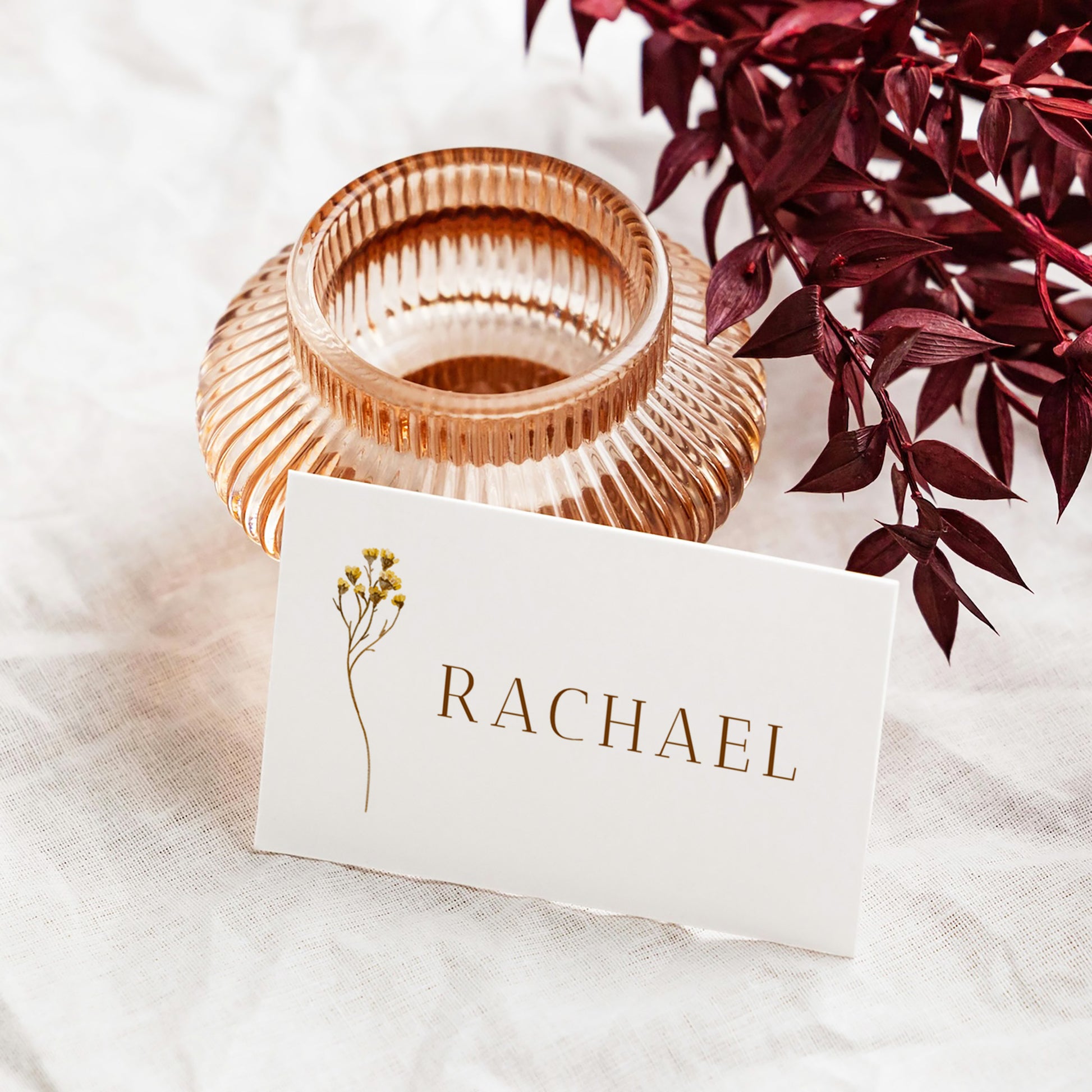 Rose gold candle holder with a flat place card leaning against it.
