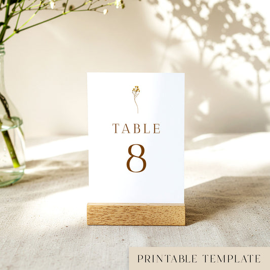 A printable table number template displayed on a small wooden block holder on a table with decorative items in the background.