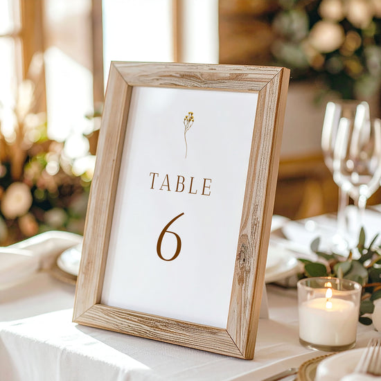 Wooden photo frame with a printed table number on a table setting with candles and glasses.
