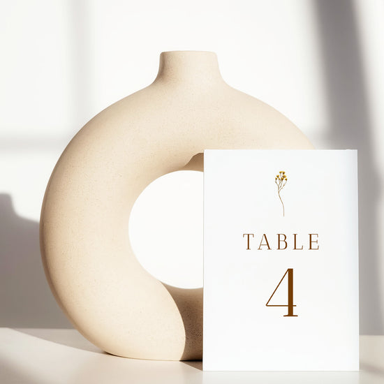 Beige ceramic circle vase with a white card displaying a table number on a light background.