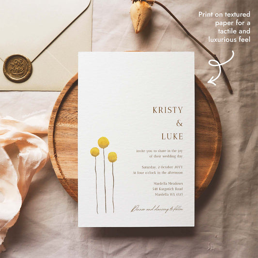 Wedding invitation template featuring three yellow billy button wildflowers, resting on a round wooden tray beside a wax-sealed envelope, printable on textured paper for a tactile feel.