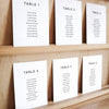 Set of six printable seating chart cards with names on a wooden display shelf.
