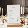 Wedding menu card on a wooden stand with candles and flowers in the background.
