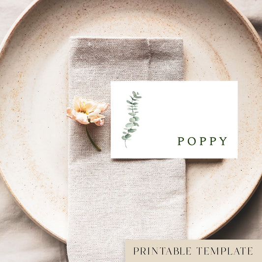 A flat place card with a name printed on it, positioned on a plate with a napkin and a floral decoration.