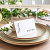 A folded place card with a name printed on it sitting on top of two plates with a eucalyptus leaf for decoration.