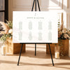 Modern seating chart template on an easel with floral arrangements and candles in a decorative setting.