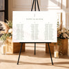 Modern seating chart template on an easel with floral arrangements and candles in a decorative setting.