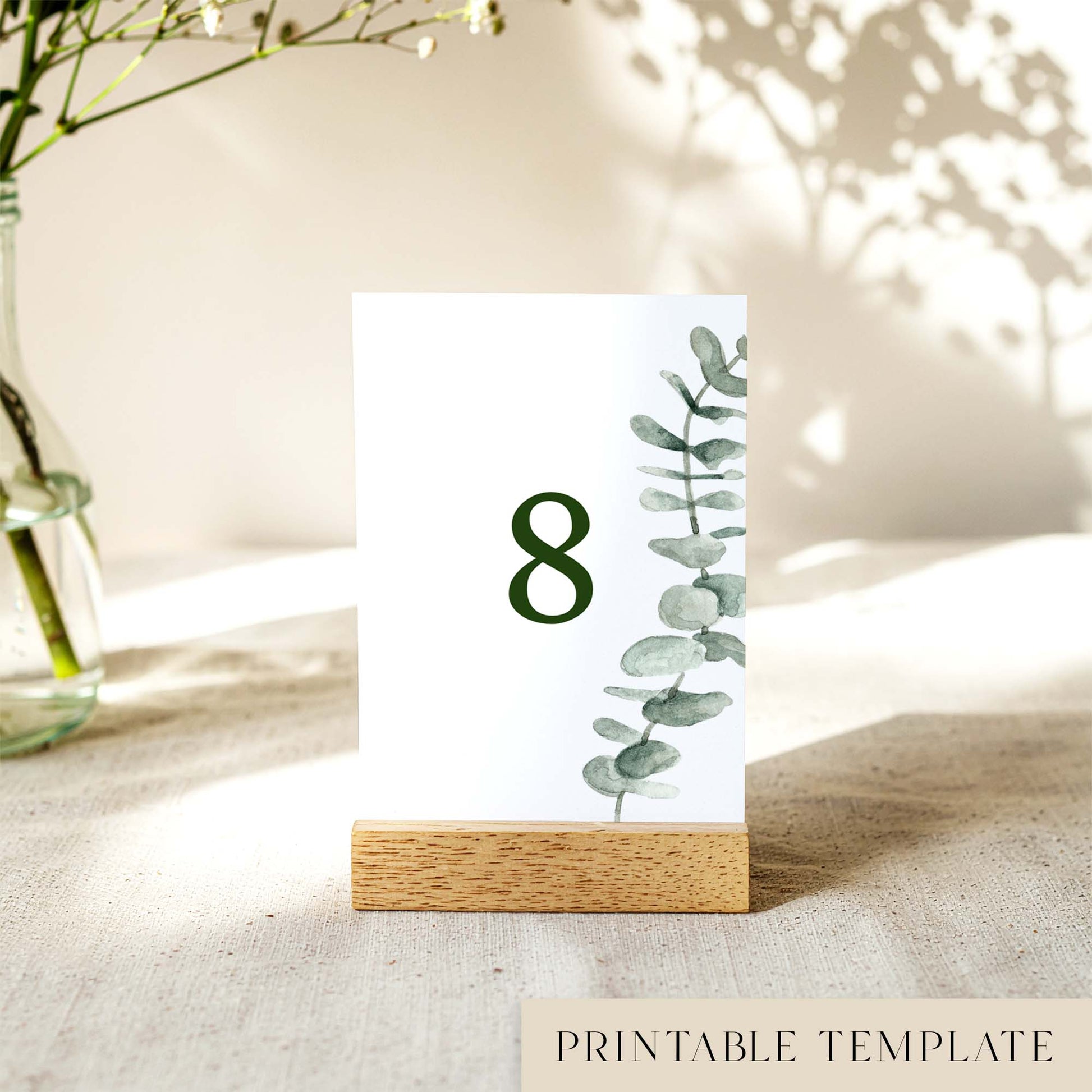 A printable table number template displayed on a small wooden block holder on a table with decorative items in the background.