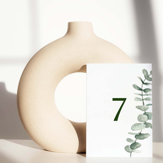 Beige ceramic circle vase with a white card displaying a table number on a light background.