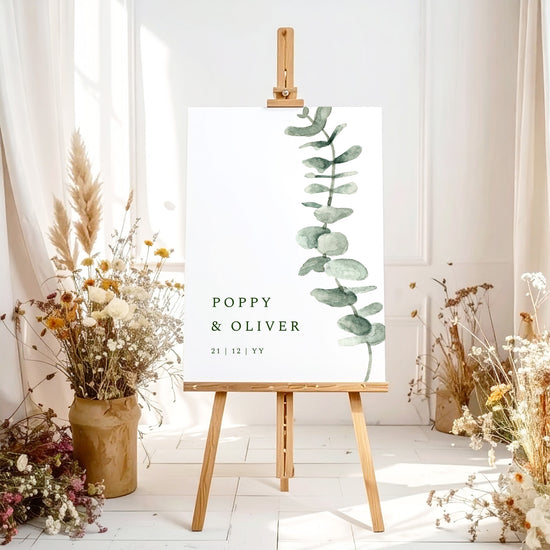 Printable wedding welcome sign template with greenery on an easel with floral arrangements in a room setting.