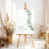 Printable wedding welcome sign template with greenery on an easel with floral arrangements in a room setting.