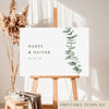 A horizontal printable wedding welcome sign template displayed on a wooden easel with a decorative dried plant in the background.