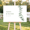 Horizontal wedding welcome sign on an easel with a blurred outdoor ceremony background.