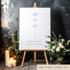 Printable minimal wedding welcome sign on an easel with floral arrangements in a room setting.