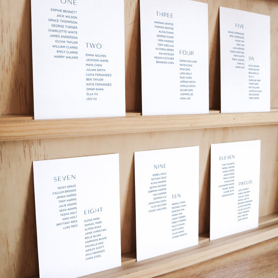 Set of six printable seating chart cards with names on a wooden display shelf.