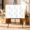 Modern long tables seating chart template on an easel with floral arrangements and candles in a decorative setting.