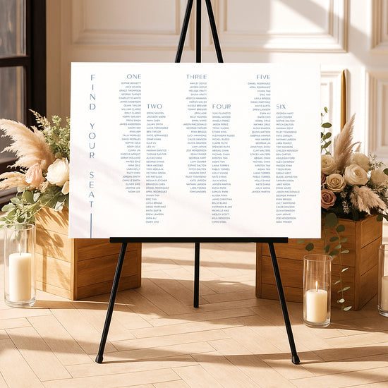 Modern long tables seating chart template on an easel with floral arrangements and candles in a decorative setting.