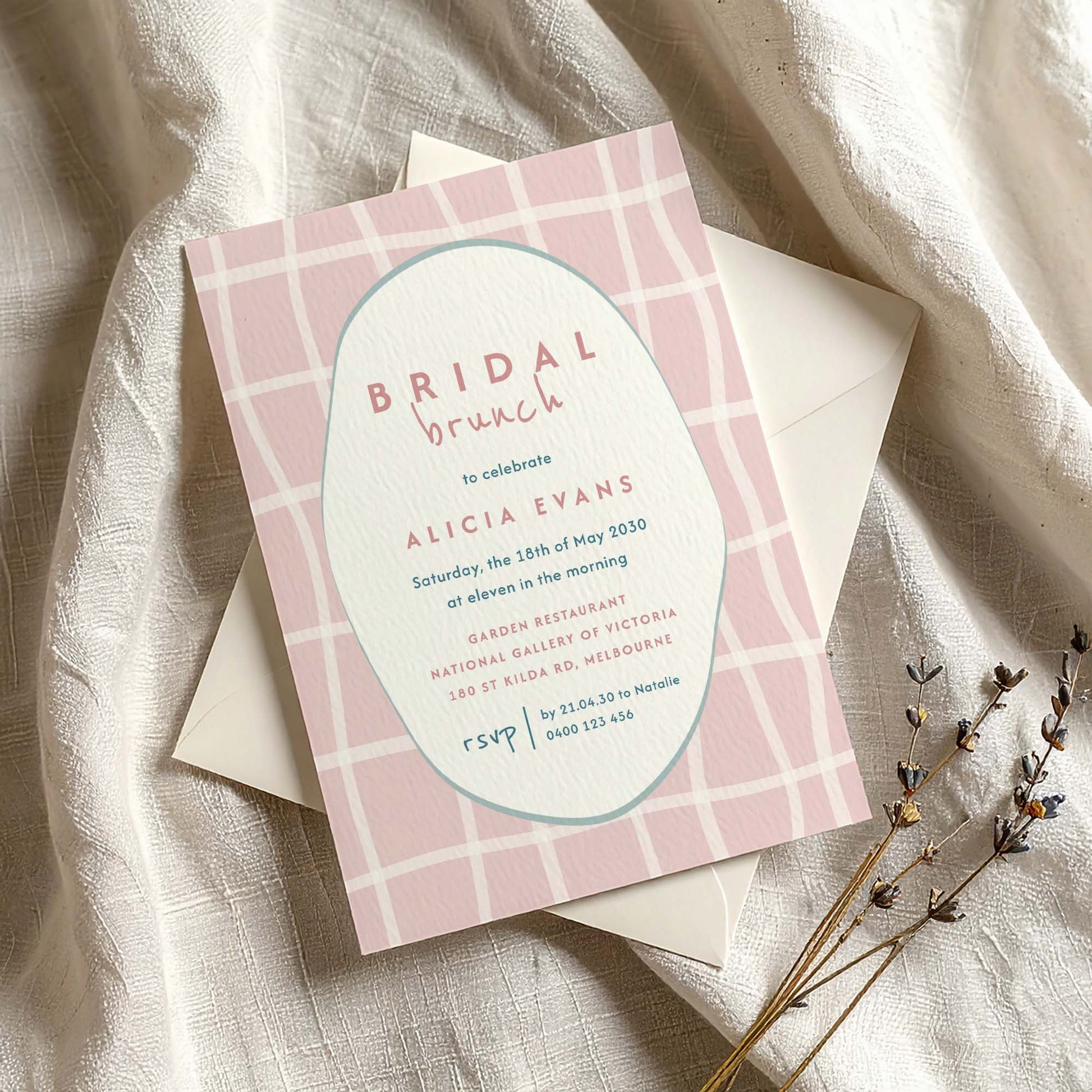 Whimsical pink bridal shower invitation on textured card with envelope on fabric background.