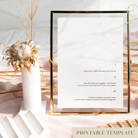 Printable wedding menu template in a gold frame on a soft pink tablecloth with dried florals and modern decorative accents.
