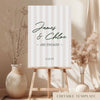 Modern stripe engagement party welcome sign on an easel with floral arrangements in a room setting.