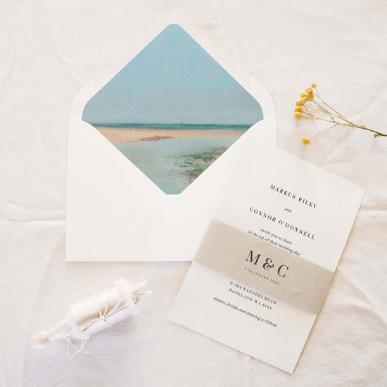 Wedding invitation set with ocean design on the envelope and beige invitation belly band.