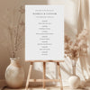 Wedding order of events sign on a stand with decorative vases and plants in the background