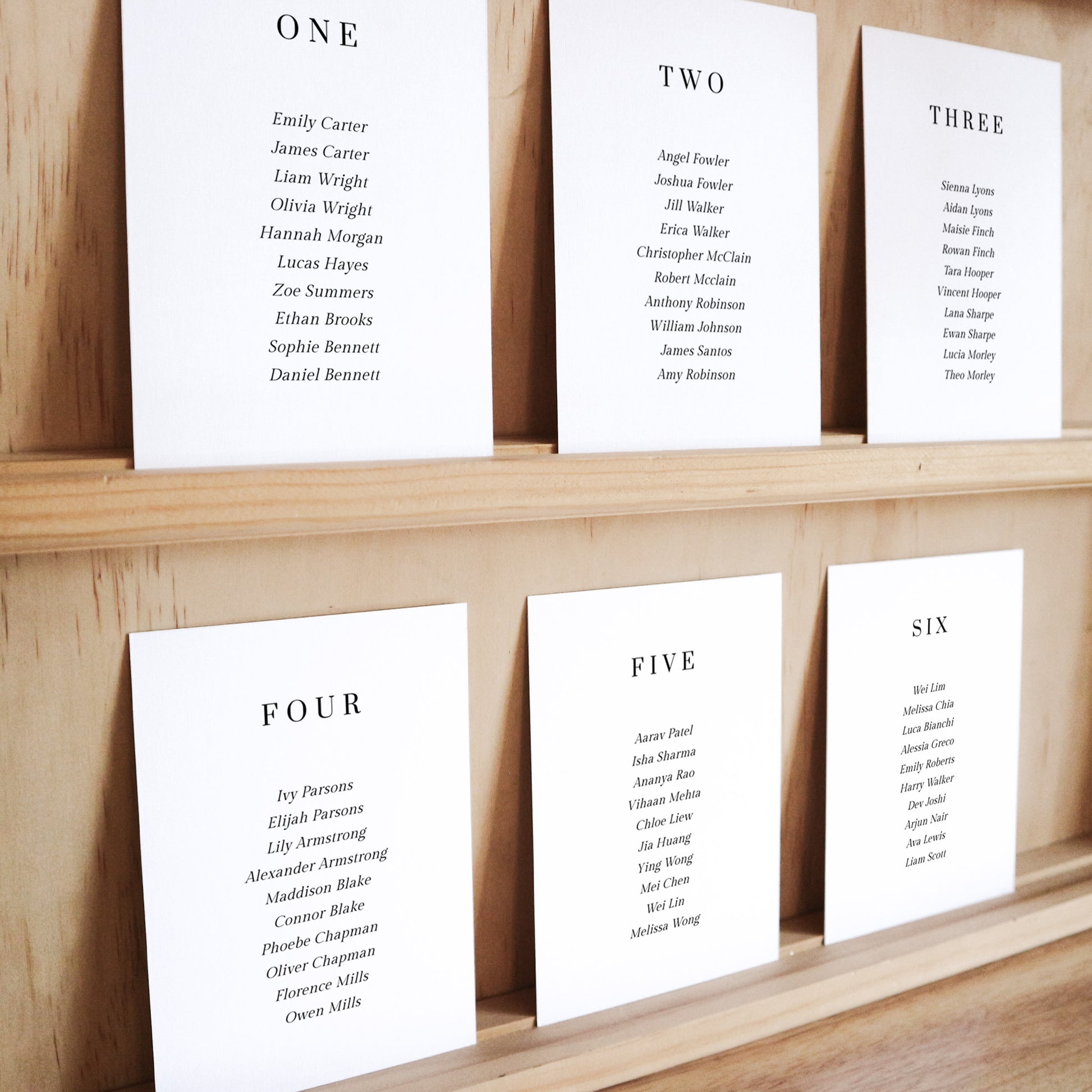 Set of six printable seating chart cards with names on a wooden display shelf.