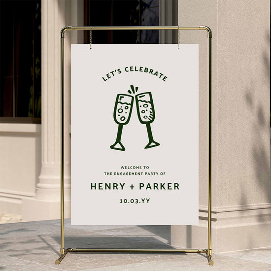 Informal engagement party welcome sign displayed on a gold stand against a neutral wall.