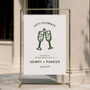 Informal engagement party welcome sign displayed on a gold stand against a neutral wall.