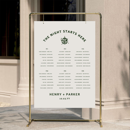 6-table wedding seating plan on a gold stand against a neutral wall.