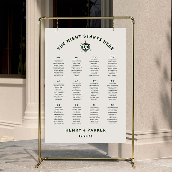 Editable 12-table wedding seating chart poster on a gold stand against a neutral wall.