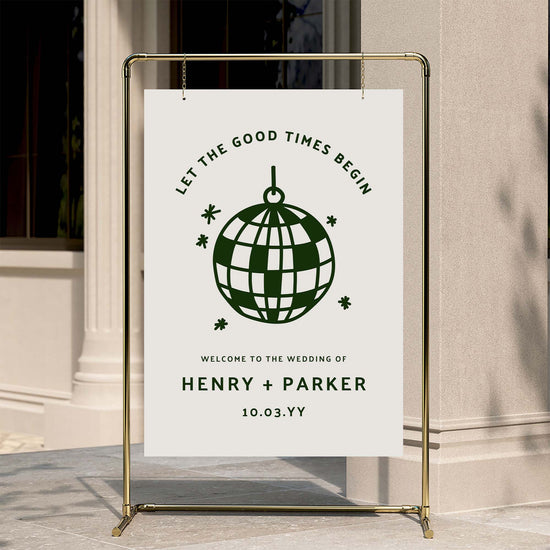 Retro-style wedding welcome sign with playful curved text and graphic disco ball detail, displayed on a gold stand against a warm neutral wall.