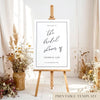 Printable bridal shower welcome sign on an easel with floral arrangements in a room setting.
