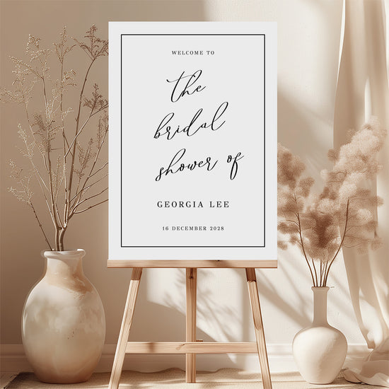 Printable bridal shower welcome sign on an easel with floral arrangements in a room setting.
