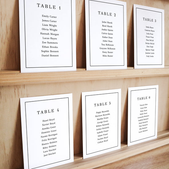 Set of six printable seating chart cards with names on a wooden display shelf.