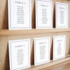 Set of six printable seating chart cards with names on a wooden display shelf.