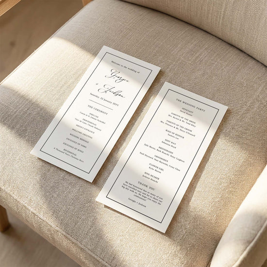 Two DL-sized wedding program cards laid flat on a cushioned chair with sunlight streaming across the linen fabric.