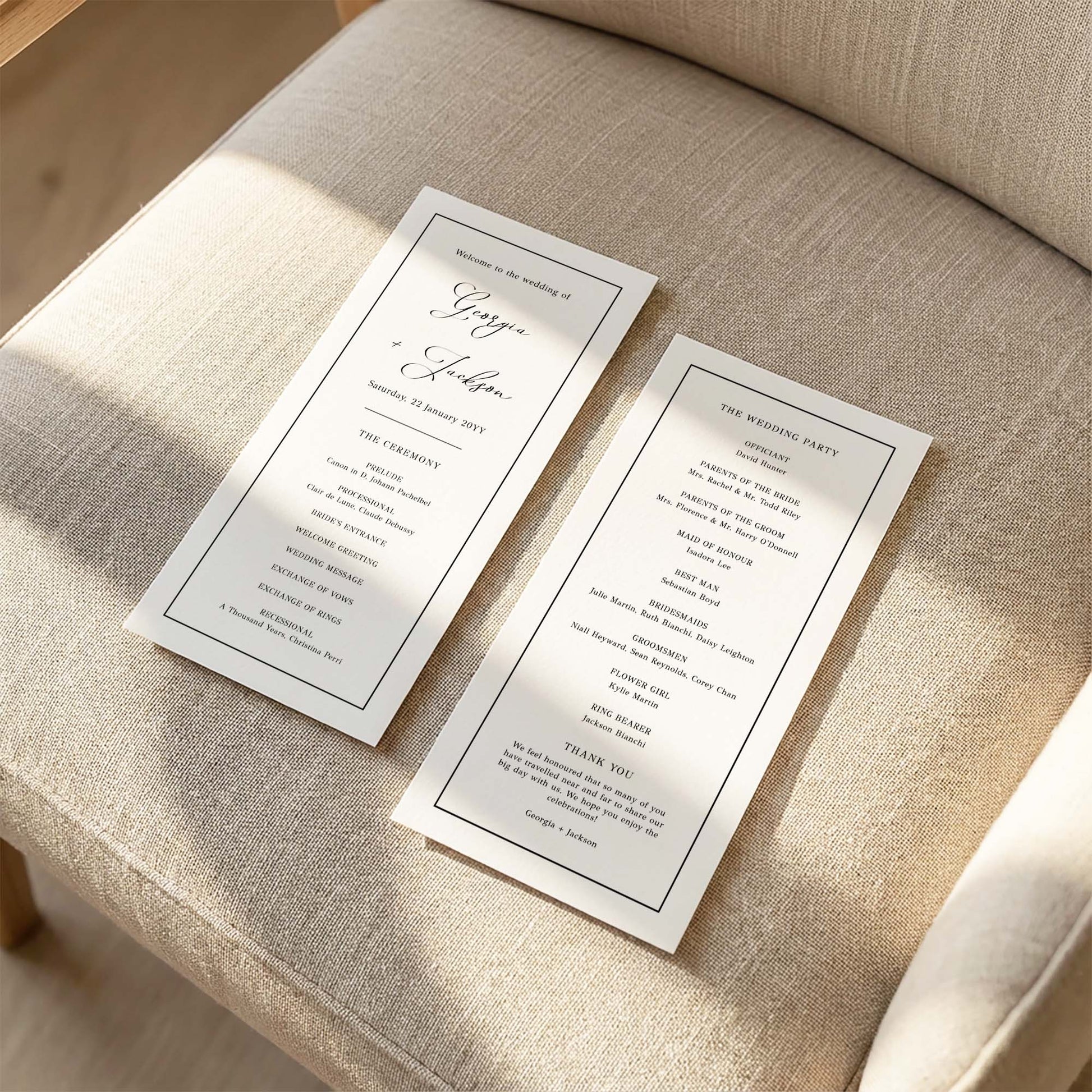 Two DL-sized wedding program cards laid flat on a cushioned chair with sunlight streaming across the linen fabric.