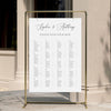 Alphabetical wedding seating chart template displayed on a gold stand against a neutral wall.
