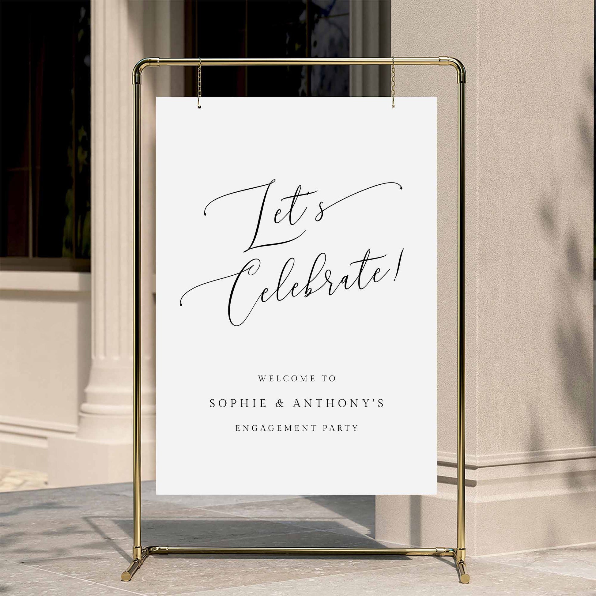 Elegant engagement party welcome sign displayed on a gold stand against a neutral wall.
