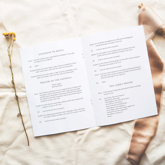 Open A5 wedding Mass ceremony booklet displaying interior ceremony text on a neutral fabric background.