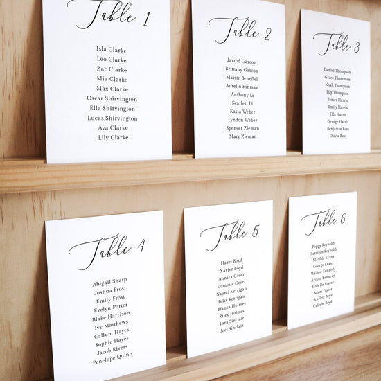 Set of six printable seating chart cards with names on a wooden display shelf.