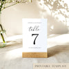 Printable table number card displayed on a wooden stand on a linen table cloth.