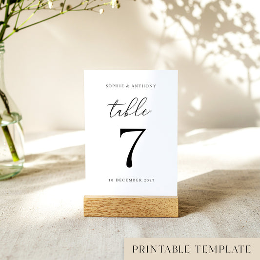 Printable table number card displayed on a wooden stand on a linen table cloth.
